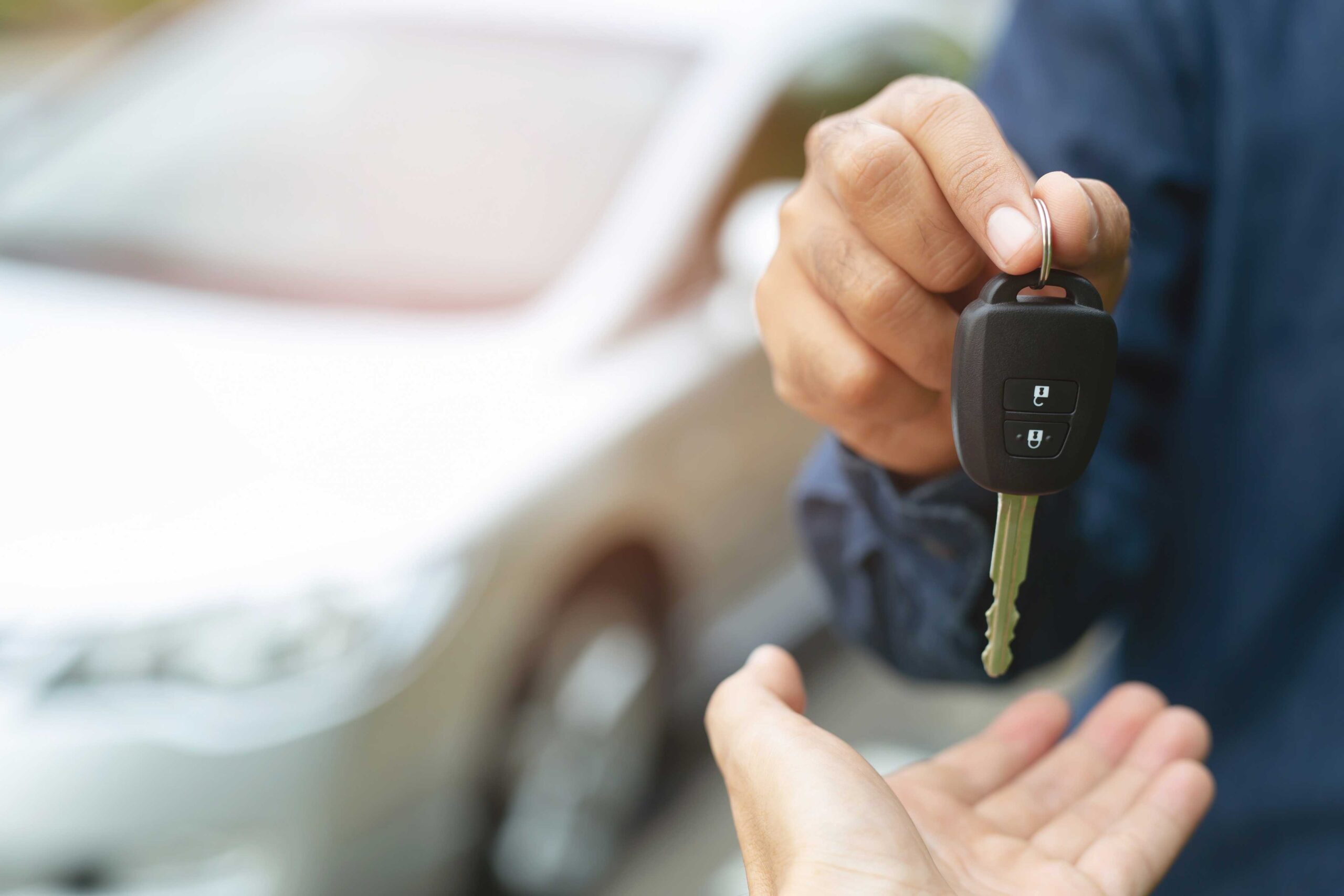 Two people exchanging car keys with silver car in the background highlighting importance of car rental excess insurance.