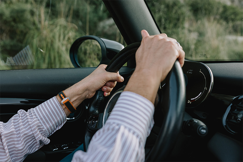 Man wearing a striped shirt has his hands on the steering wheel of a car protected with a hire car excess insurance policy.